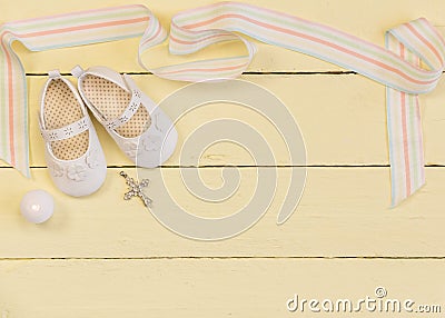 Christening background with white shoes, candle and crystal cross pendant on yellow painted wooden background Stock Photo