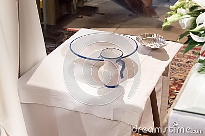 Christening objects prepared on a table inside a church. Jug with blessed water, basin and shell. Stock Photo