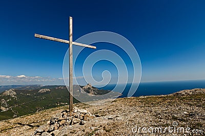 Christian wooden cross on mountain top, rocky summit, beautiful inspirational landscape with ocean, clouds and blue sky Stock Photo