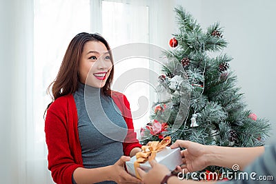 Christmas Asian Couple. A handsome man giving her girlfriend/wife a gift at home celebrating New Year People Stock Photo