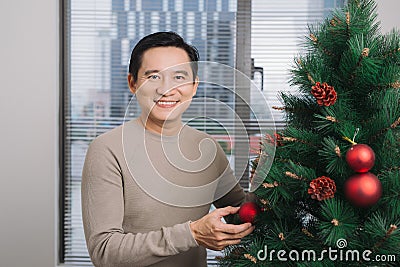 Christmas. Asian man standing new christmas tree at home celebrating New Year. Stock Photo