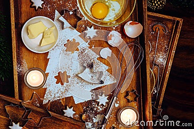 Christmas baking composition, fir tree shape from flour, butter, egg and cinnamon stars, utensils and candles on warm brown wooden Stock Photo