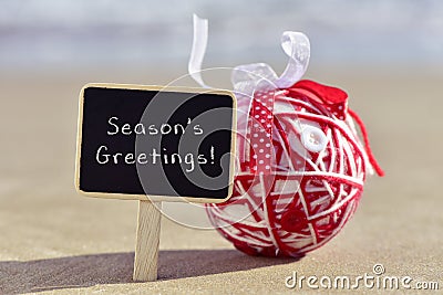 Christmas ball and text seasons greetings on the beach Stock Photo