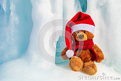 Christmas bear in a Santa Claus hat and a red knitted scarf tied around his neck. A bear sits in an ice cave in winter Stock Photo