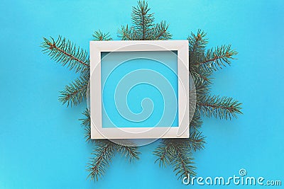 Christmas Border. Fir tree branches and white wooden frame on blue paper background. Top view. Copy space. Stock Photo