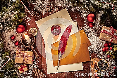 Christmas card background with letter, envelopes and vintage red feather quill pen surrounded by gifts, pine and baubles lit by a Stock Photo