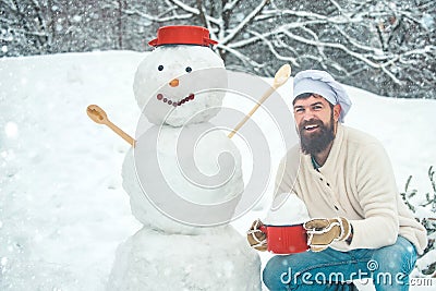 Christmas chef cook. Man in snow. Winter portrait of handsome cook in snow Garden with snowman. Stock Photo