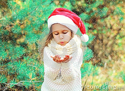 Christmas child little girl in santa red hat blowing snow lying on her hands over tree Stock Photo