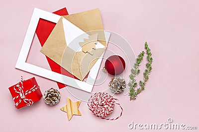 Christmas composition. Envelope with blank white paper, fir branches, cones, red ball, twine, gift, wooden toys on pink background Stock Photo