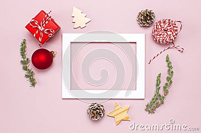 Christmas composition. White photo frame, fir branches, cones, red ball, twine, gift, wooden toys on pink background Flat lay top Stock Photo