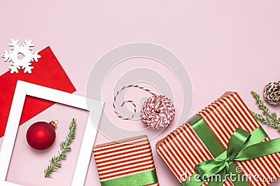 Christmas composition. White photo frame, red envelope, fir branches, cones, ball, twine, gift, wooden toys on pink background Stock Photo
