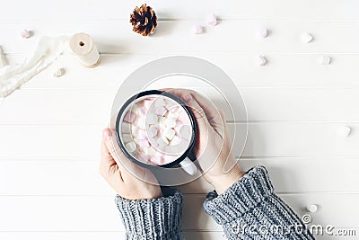 Christmas composition. Woman`s hands in sweater holding cup of hot chocolate. Marshmallows, pine cones and silk ribbon Stock Photo