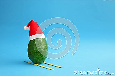 Christmas decoration background with frsh green avocado skiing in santa hat on bright blue background. Card concept. Closeup. Stock Photo