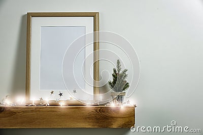 Christmas decorations in bright shiny colors with Christmas lights and frame picture. Wooden shelf and white wall background. Stock Photo