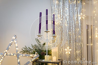 Christmas decorations. Purple candles in candlestick, fir tree branches and cones, siver curtains with shiny stars Stock Photo
