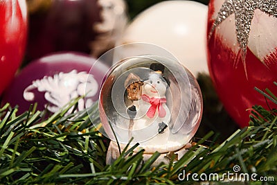 Christmas decorations. Shiny magical crystal ball with snowman and Christmas balls on tree twig. Snowing dome with xmas background Stock Photo