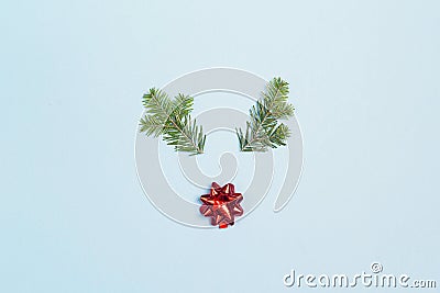 Christmas deer face made of fir-tree branches and red bow on blue background. Flat lay, top view Stock Photo