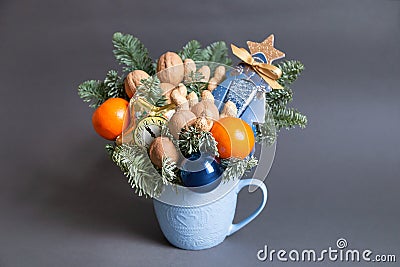 Christmas edible bouquet with nuts, tangerines, nobilis and christmas decor in a blue cup on a gray background Stock Photo