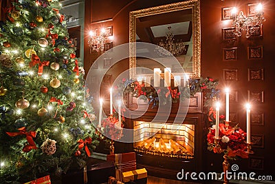 Christmas evening by candlelight. classic apartments with a white fireplace, decorated tree, sofa, large windows and Stock Photo