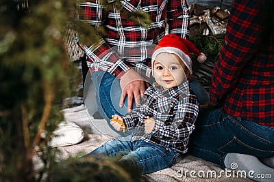 Christmas family portrait of young happy smiling parents playing with small kid in red santa hat near the christmas tree. Winter Stock Photo