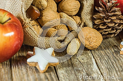 Christmas and Advent food decoration with nuts in santa claus sack, red apple, and star cookie on wooden table Stock Photo