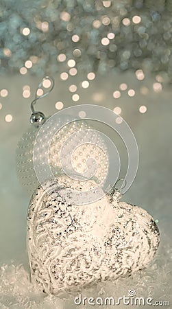 Christmas greeting card. Glass heart and a white ball with pearls on a snow. Blurred gray backdrop of yellow bokeh and light Stock Photo