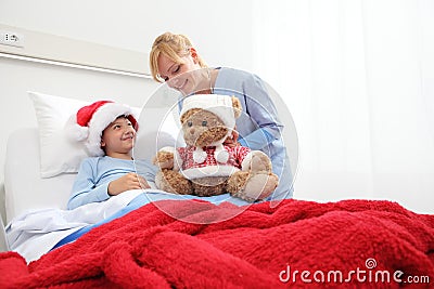 Christmas holiday in hospital happy child lying in bed with Santa Claus hat and nurse dressing a teddy bear Stock Photo
