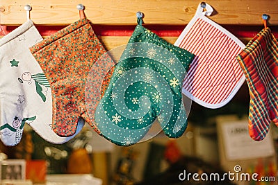 Christmas mittens potholders hang in kitchen against the background of blurry kitchen appliances. Stock Photo