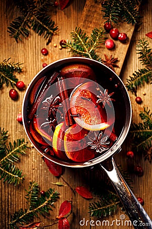 Christmas mulled red wine with the addition of spices and citrus fruits in a pot on a rustic wooden table, top view. Stock Photo