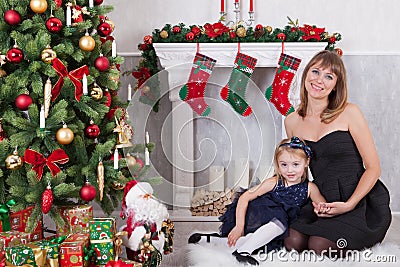 Christmas or New year celebration. Happy mother with her daughter sit near a white fireplace next to a christmas tree Stock Photo