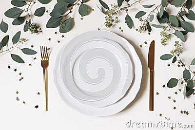 Christmas, New Year table place setting. Golden cutlery, porcelain plate, eucalyptus branches and golden confetti stars Stock Photo