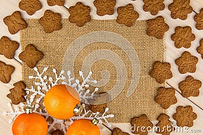 Christmas or New Year tangerines and gingerbread cookies with snowflakes framed on brown sack background texture. Stock Photo