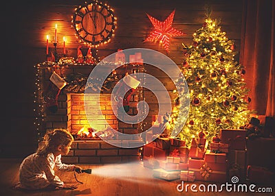 Christmas night. baby girl with a flashlight at night looking for gifts under Christmas tree Stock Photo