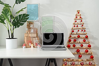 Christmas online shopping. Laptop and gifts on a white desk, original Christmas tree from branches in a home office. Stock Photo