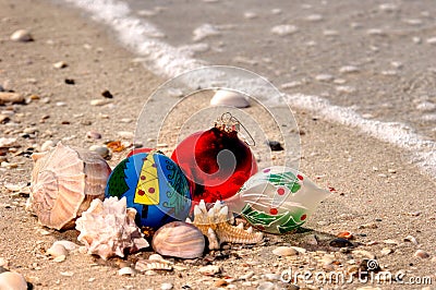 Christmas ornaments and shells on a sandy beach with a wave along the Gulf of Mexico for the holiday. Stock Photo