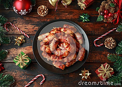 Christmas Pigs in blankets, sausages wrapped in bacon with decoration, gifts, green tree branch on wooden rustic table Stock Photo