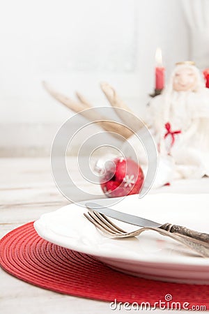 Christmas place setting with white dishware, cutlery, silverware and red decorations on wooden board. Christmas Stock Photo