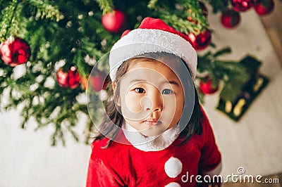 Christmas portrait of adorable 3 year old asian toddler girl wearing red Santa dress and hat Stock Photo