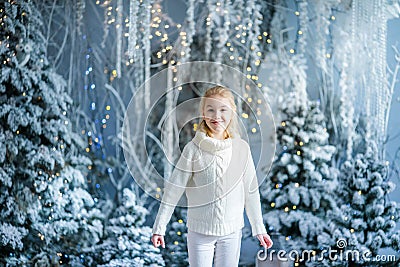 Christmas portrait of happy blonde child girl ndoor studio, snowy winter decorated tree on background. New Year Holidays Stock Photo