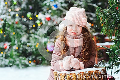 Christmas portrait of happy kid girl playing outdoor in snowy winter day, fir trees decorated for New Year holidays Stock Photo