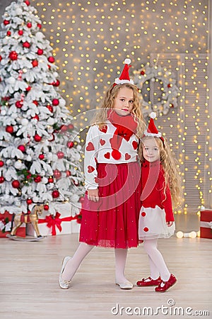 Christmas portrait of two beautyful cute girls Smiling sisters friends and xmas luxury green white tree in unique interior studio Stock Photo