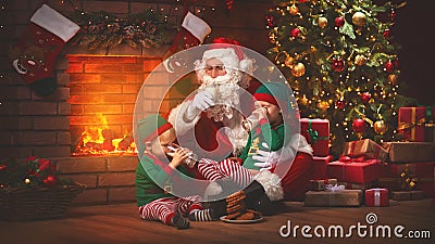 Christmas. Santa Claus with Elves Drink Milk and Eat Cookies Stock Photo