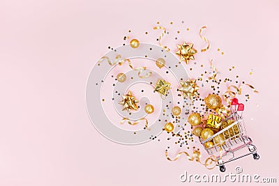 Christmas shopping cart with gift, holiday decorations and golden confetti on pink pastel background top view. Flat lay style. Stock Photo