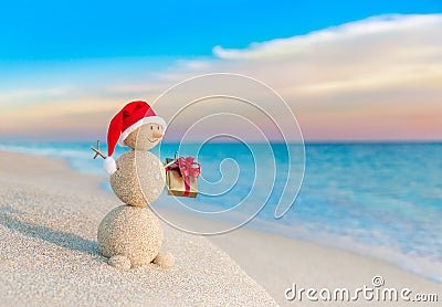 Christmas Snowman in Santa hat with gift at sunset beach Stock Photo