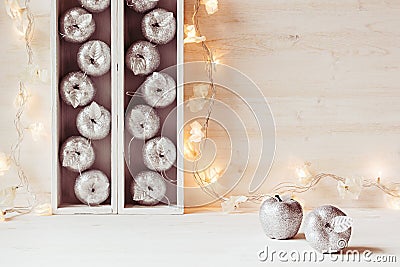 Christmas soft home decor of silver apples and lights burning in boxes on a wooden white background. Stock Photo