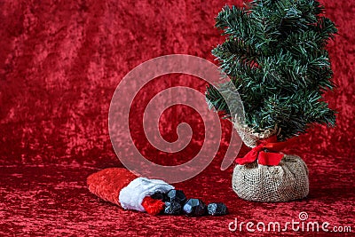 Christmas stocking spilling out coal candy, for bad boys and girls, with a burlap ball artificial tree, on a red background Stock Photo