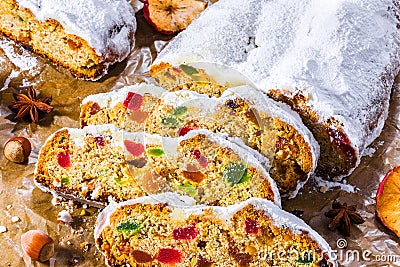 Christmas Stollen. Traditional Sweet Fruit Loaf with Icing Sugar on the parchment paper with hazelnuts, dry sliced apple, cinnamon Stock Photo