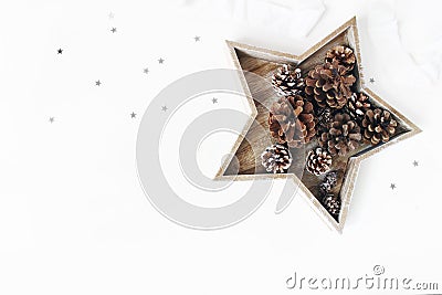 Christmas styled table composition. Pine and larch cones in star shaped wooden tray, silver confetti and silk ribbon Stock Photo