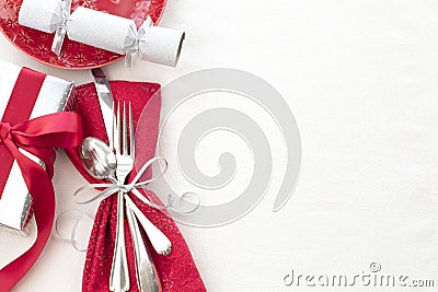 Christmas Table Place Setting in Red, White and Silver with Silverware, a gift, and party cracker on White Cloth Background with r Stock Photo