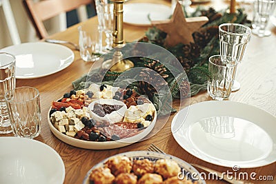 Christmas table setting. Modern cheese platter with cranberry sauce as christmas tree, fir branches and pine cones, candles, Stock Photo